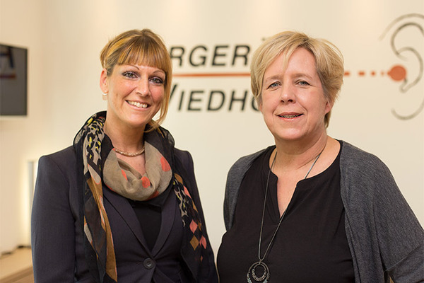 Zwei freundliche Frauen stehen in einem modernen Hörakustik-Fachgeschäft.